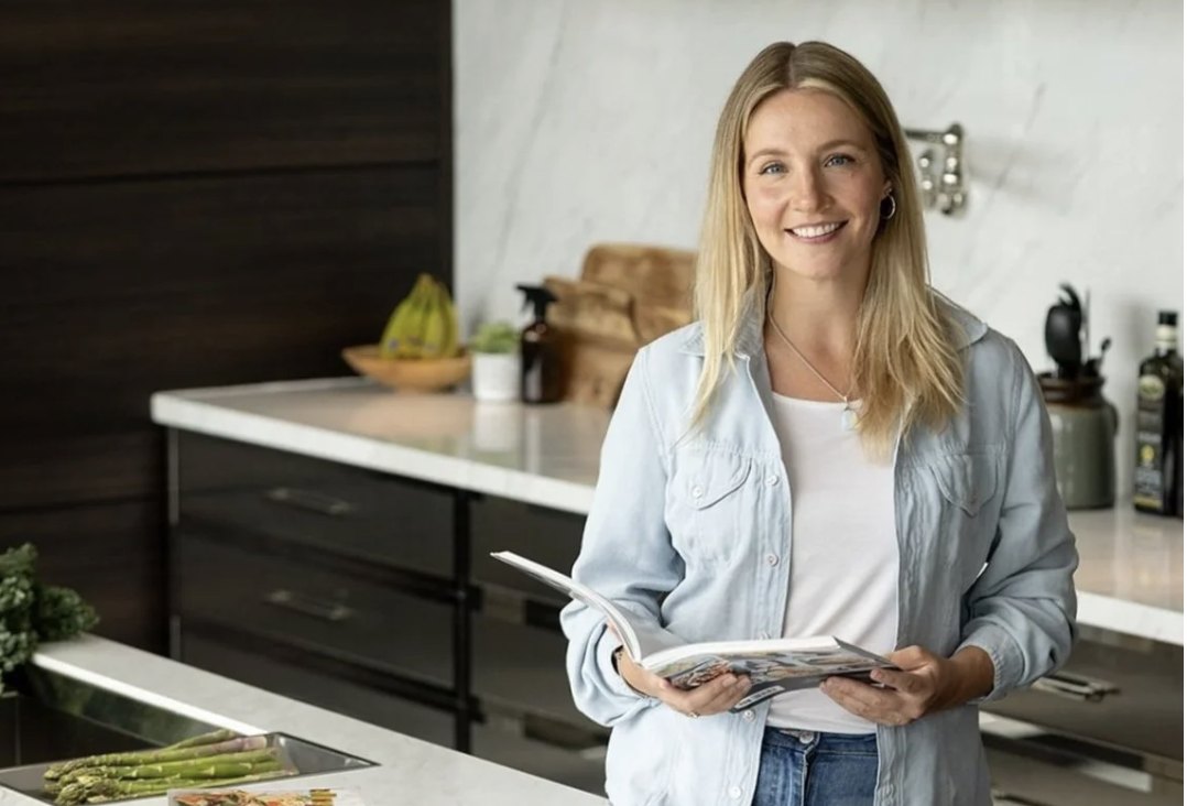 Allysa holding an open recipe book in a bright kitchen